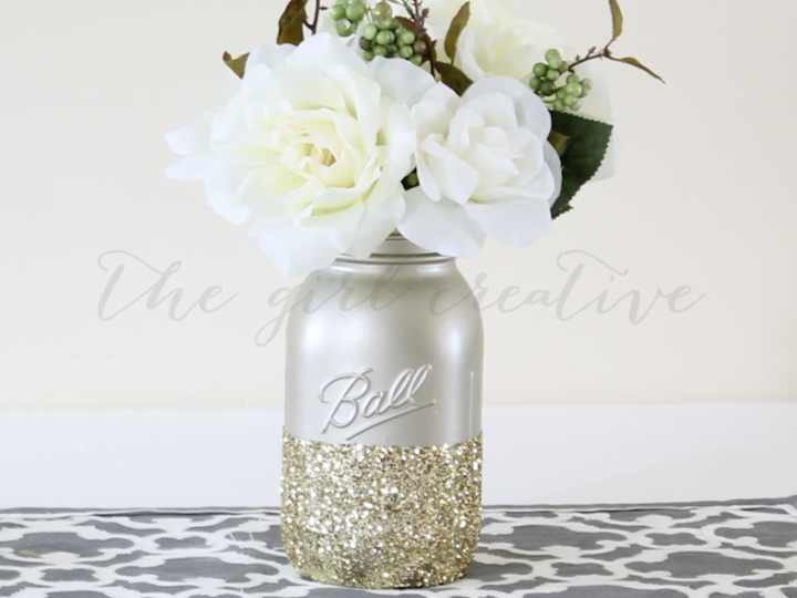 Gold spray pained mason jar dipped in gold glitter with faux flowers on table