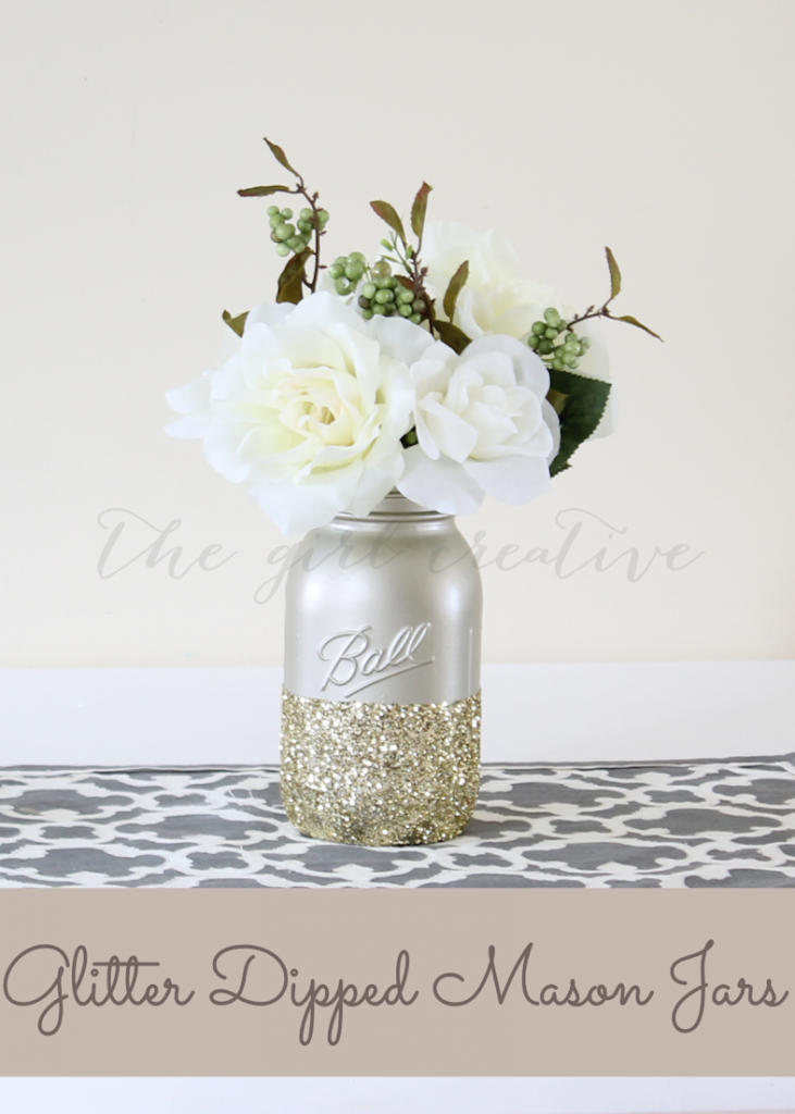 Gold spray pained mason jar dipped in gold glitter with faux flowers on table